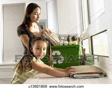 Stock Photo - Girl (4-6) helping mother recycle newspapers, smiling, portrait. Fotosearch