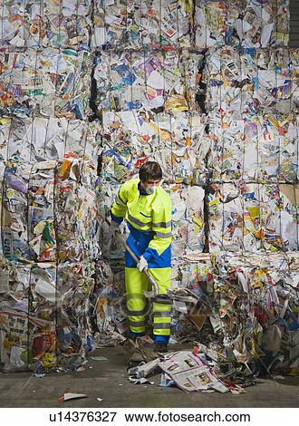 Stock Photo - Man shoveling in front of a wall of recycling.. Fotosearch