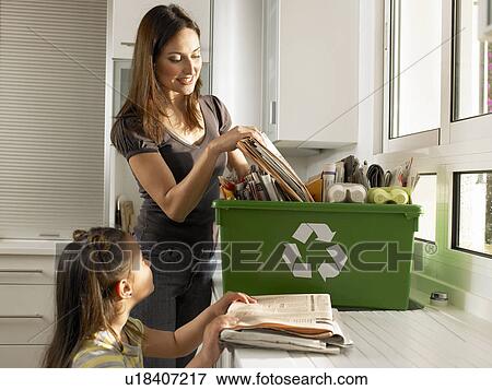 Stock Photo - Mother and daughter (4-6) filling recycling box, smiling. Fotosearch