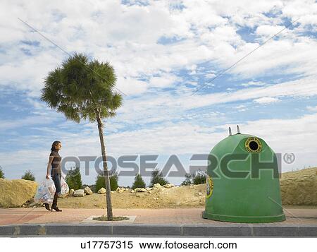 Woman walking along sidewalk/pavement carrying recycle objects toward recycle bin View Large Photo Image Stock Photography - Woman walking along sidewalk/pavement carrying recycle objects toward recycle bin. Fotosearch