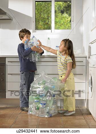 Stock Image - Young boy (6-8) and girl 4-6) sharing recycling duties in kitchen. Fotosearch