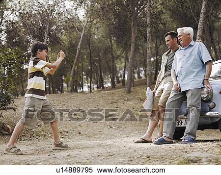 Boy (8-10) photographing father and grandfather leaning against car bonnet View Large Photo Image Stock Photography - Boy (8-10) photographing father and grandfather leaning against car bonnet. Fotosearch