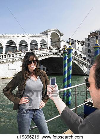 Stock Photography - Man taking photograph of woman by Rialto Bridge. Venice, Italy.. Fotosearch