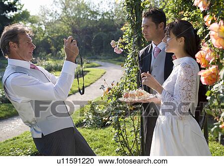 Mature father photographing bride and groom in garden View Large Photo Image Stock Image - Mature father photographing bride and groom in garden. Fotosearch