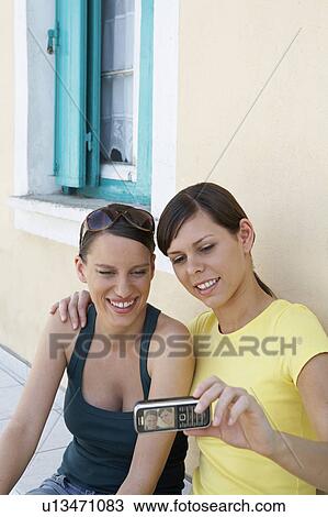 Stock Image - Two young girls outside a Greek House taking a self portrait with mobile smiling. Fotosearch