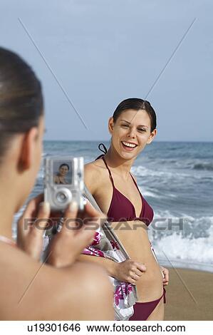 Stock Photograph - Two young women on beach taking photos.. Fotosearch