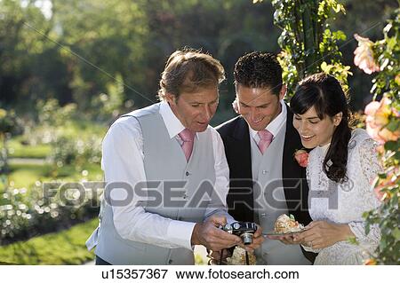 Stock Photo - Young bride and groom and mature father looking at camera, smiling. Fotosearch