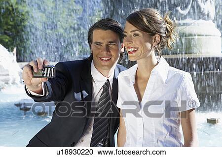 Stock Image - Young couple taking picture together beside fountain.. Fotosearch