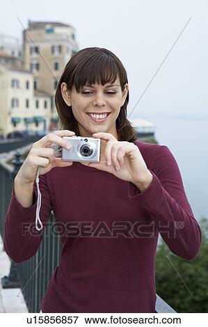 Stock Photo - Young woman portrait with camera taking a picture smiling old city in background.. Fotosearch