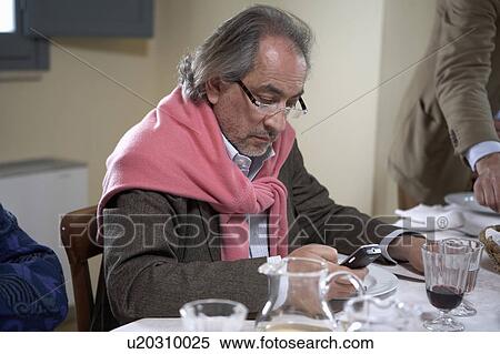 Stock Photography - Mature man text messaging at dinner table. Fotosearch