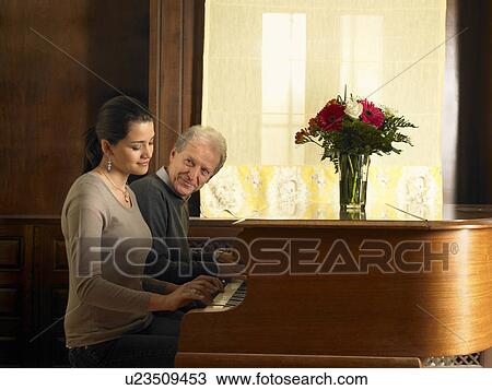 Stock Image - Senior father and daughter playing duet at piano, smiling. Fotosearch