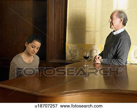 Stock Photo - Senior father watching daughter playing piano, smiling. Fotosearch
