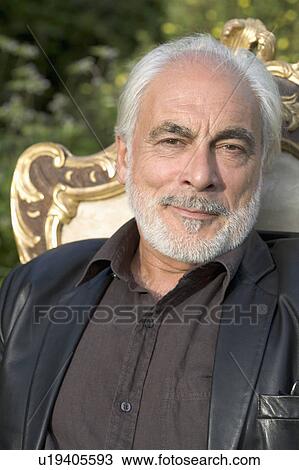 Stock Image - Senior man sitting in guilt chair in garden.. Fotosearch