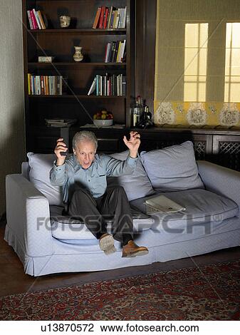Stock Image - Senior man sitting on sofa watching television, celebrating. Fotosearch