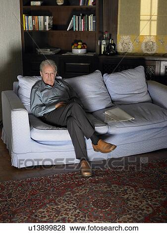 Stock Photo - Senior man sitting on sofa watching television. Fotosearch