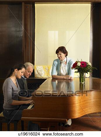 Picture - Senior parents listening to daughter playing piano. Fotosearch