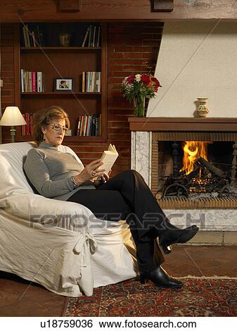 Senior woman reading book by fire in living room View Large Photo Image Stock Photograph - Senior woman reading book by fire in living room. Fotosearch