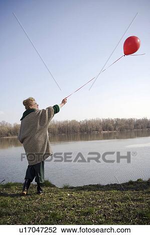 Senior woman standing by river holding red balloon, rear view View Large Photo Image Stock Image - Senior woman standing by river holding red balloon, rear view. Fotosearch