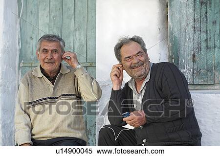 Stock Photography - Two mature men sharing earphones and laughing.. Fotosearch