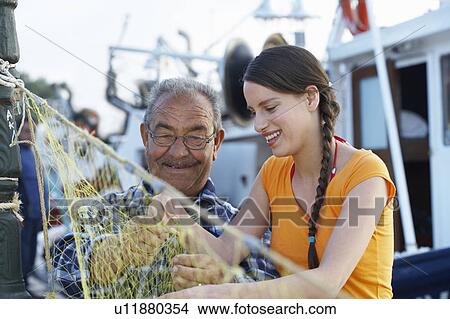 Picture - Young girl and fisherman on fishing net sewing it together little port in background.. Fotosearch