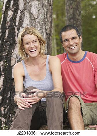 Couple sitting in a forest smiling. View Large Photo Image Stock Image - Couple sitting in a forest smiling.. Fotosearch