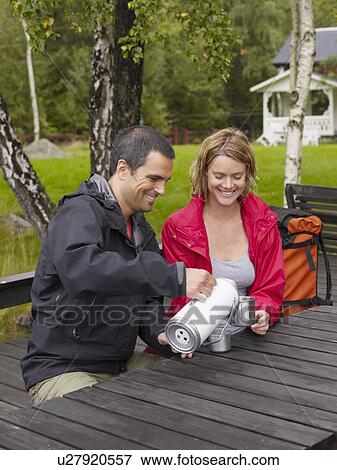 Couple sitting in a park with a thermos smiling. View Large Photo Image Stock Photo - Couple sitting in a park with a thermos smiling.. Fotosearch
