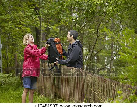 Stock Photo - Man handing laughing woman backpack over a fence.. Fotosearch