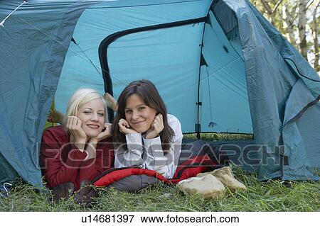 Stock Photo - Two women lying in a tent at campsite smiling.. Fotosearch
