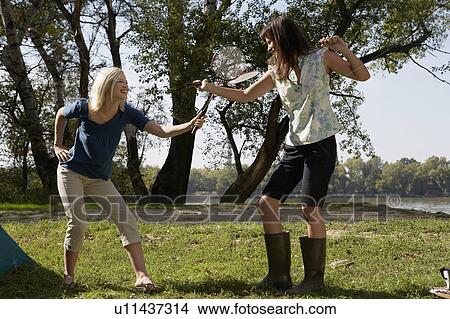 Two women play fighting with badminton racquets and laughing at campsite. View Large Photo Image Picture - Two women play fighting with badminton racquets and laughing at campsite.. Fotosearch