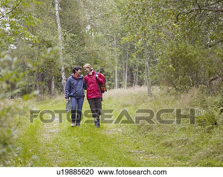 Stock Image - Two women walking through a forest with a map smiling.. Fotosearch