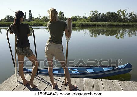 Stock Image - Two young women standing on pier with oars.. Fotosearch