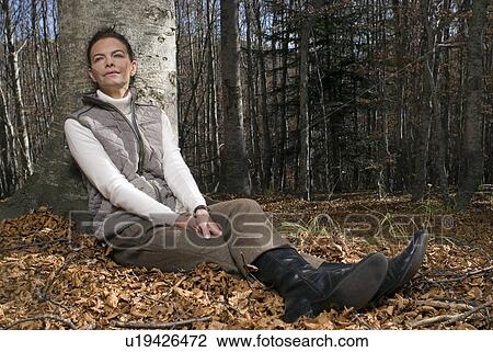 Stock Image - Woman leaning against a tree smiling.. Fotosearch