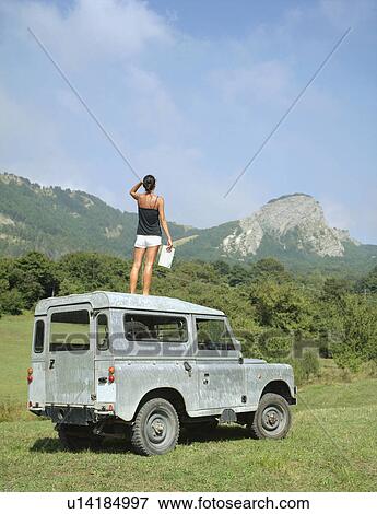 Stock Photo - Woman standing on roof of SUV holding map.. Fotosearch