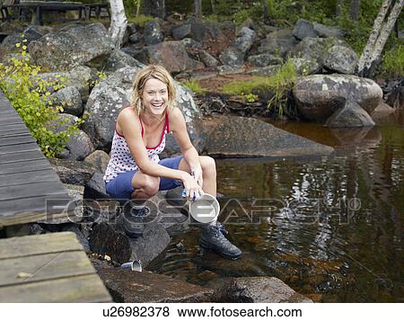 Stock Photo - Woman washing a bowl in the water by a dock smiling.. Fotosearch