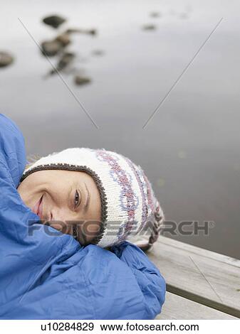 Stock Photo - Woman with on a dock in a sleeping bag smiling.. Fotosearch