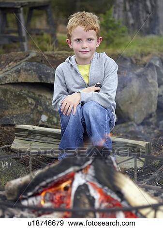 Young boy sitting by fire pit holding a hot dog. View Large Photo Image Stock Photo - Young boy sitting by fire pit holding a hot dog.. Fotosearch