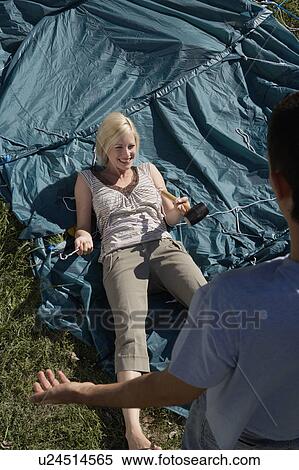 Stock Photography - Woman holding mallet lying on unraised tent laughing with man standing nearby.. Fotosearch