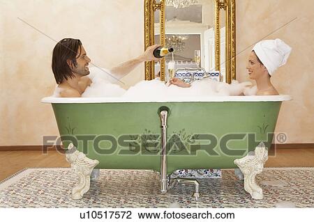Stock Image - young couple sitting in bath drinking champagne, side view. Fotosearch