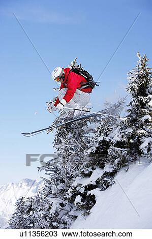 Stock Image - Austria, Saalbach, male skier jumping through trees on slope. Fotosearch