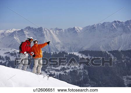 Stock Image - Austria, Saalbach, two male skiers on mountain slope, one pointing. Fotosearch