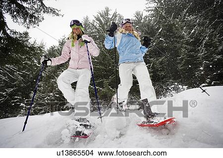 Low angle view of two young blonde women walking down small hill in forest using snow-shoes View Large Photo Image Picture - Low angle view of two young blonde women walking down small hill in forest using snow-shoes. Fotosearch