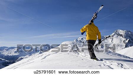 Male skier walking over mountain ridge carrying skis, rear view View Large Photo Image Stock Image - Male skier walking over mountain ridge carrying skis, rear view. Fotosearch