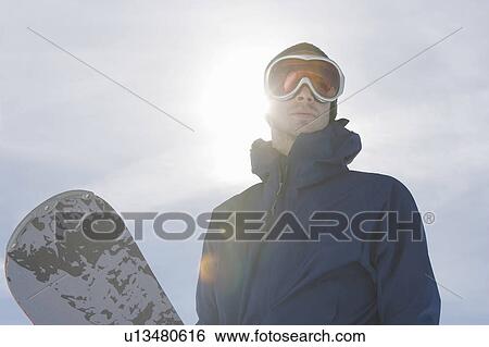 Stock Photograph - Male snowboarder with snowboard against sun, portrait. Fotosearch