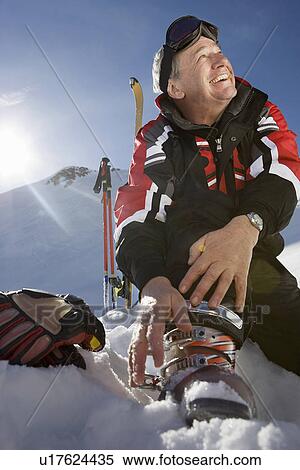 Stock Photography - Mature male skier fastening boot bindings on mountain. Fotosearch