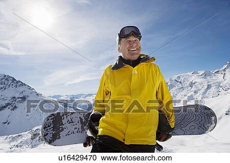 Stock Image - Mature male snowboarder with snowboard on mountain, portrait. Fotosearch