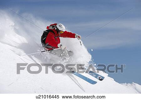 Stock Photography - Austria, Saalbach, man skiing on slope sending up snow spray. Fotosearch