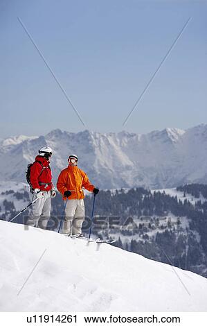 Stock Image - Austria, Saalbach, two skiers standing on slope talking to each other. Fotosearch