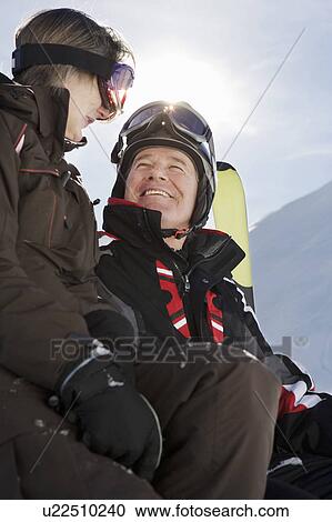 Stock Image - Mature couple in ski-wear holding Skis on mountain, close-up, low angle view. Fotosearch