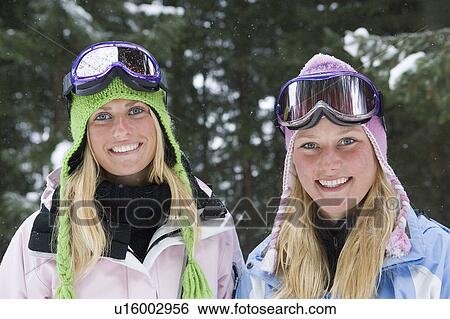 Stock Photograph - Portrait of two young blonde women wearing ski-wear in forest. Fotosearch