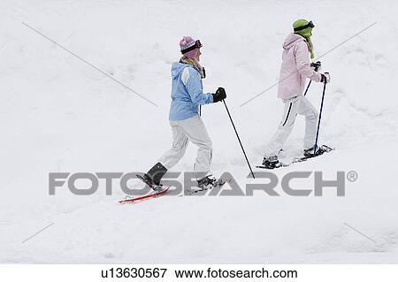 Stock Photo - Side view of two young women woman walking in snow-shoes, side view. Fotosearch